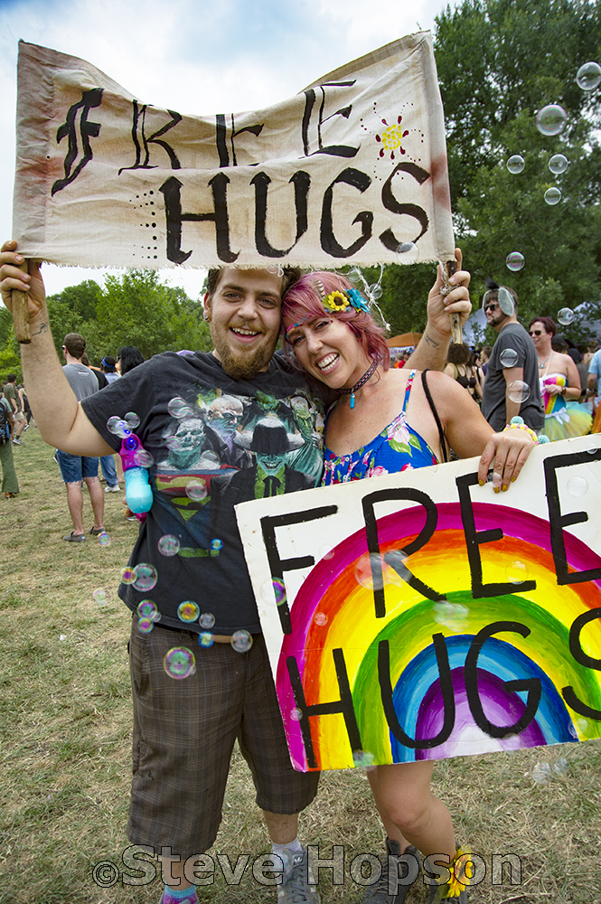 A cheerful pair holds signs saying "Free Hugs," with colorful artwork and bubbles floating around them at Eeyore's.