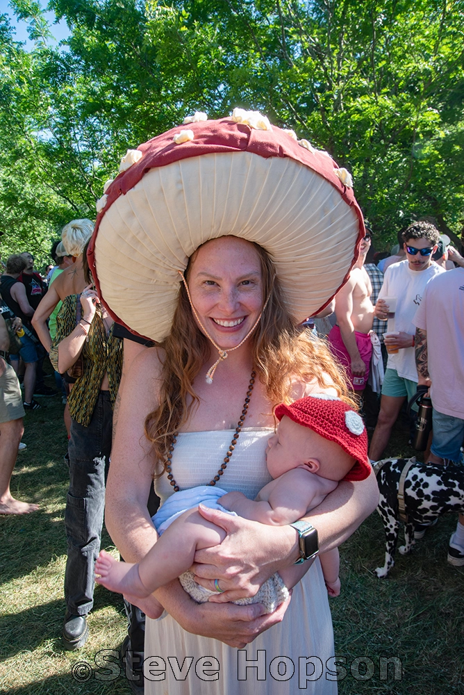 A woman wearing a large mushroom hat cradles a baby in a red mushroom cap while smiling at Eeyore's.